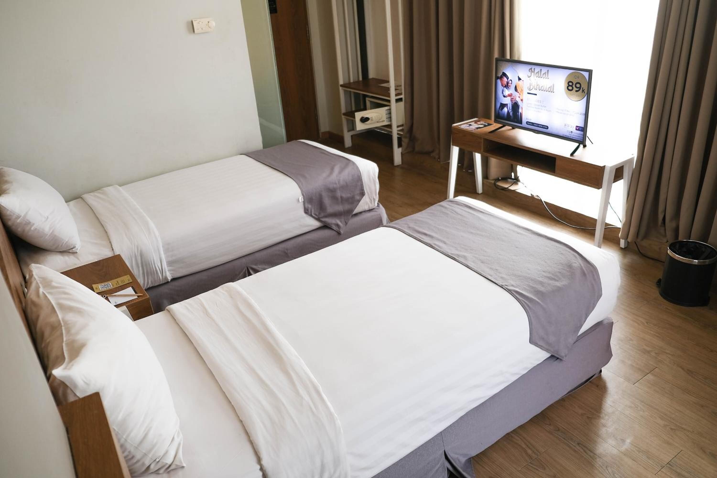 Habitación de hotel con dos camas, un escritorio con televisor y una ventana con cortinas.