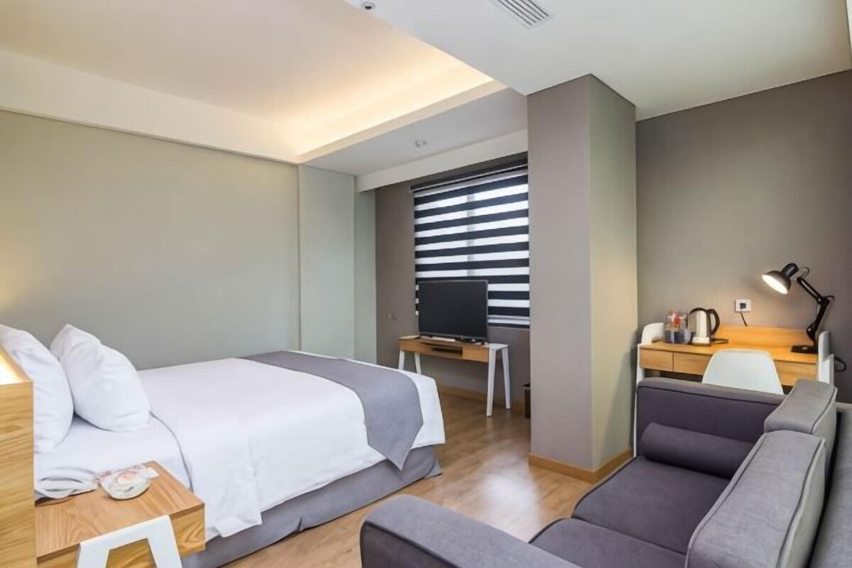 A hotel room with a bed, a desk, a chair, and a sofa.
