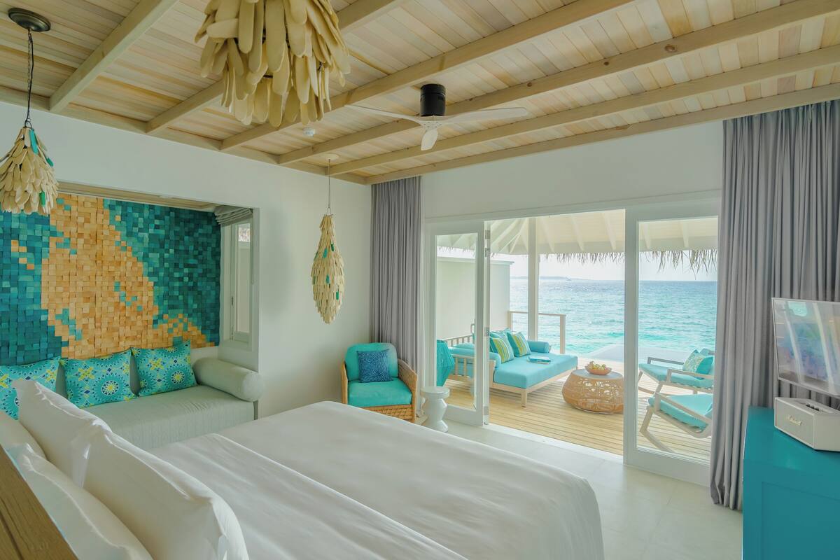 Une chambre avec un grand lit, une vue sur l’océan et un balcon aménagé avec des sièges.