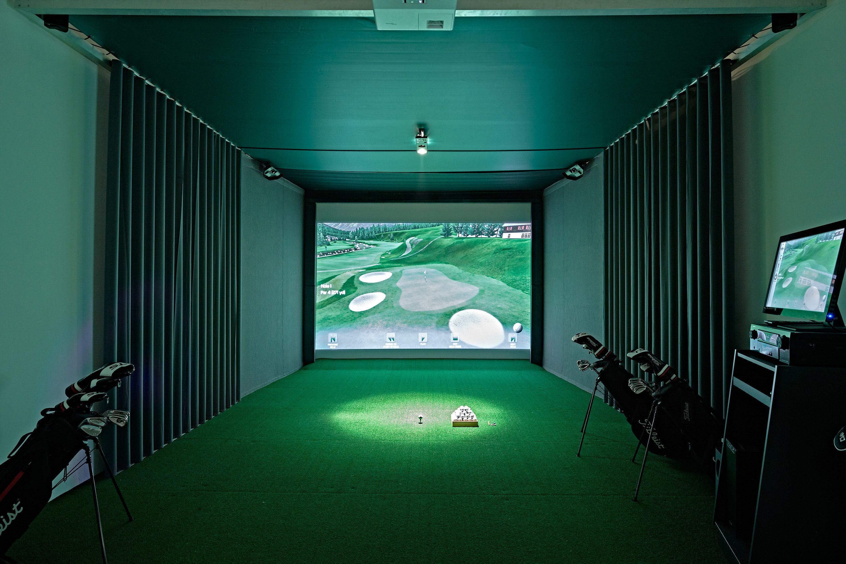 A room with a large screen displaying a golf course, a golf bag, and a golf cart.