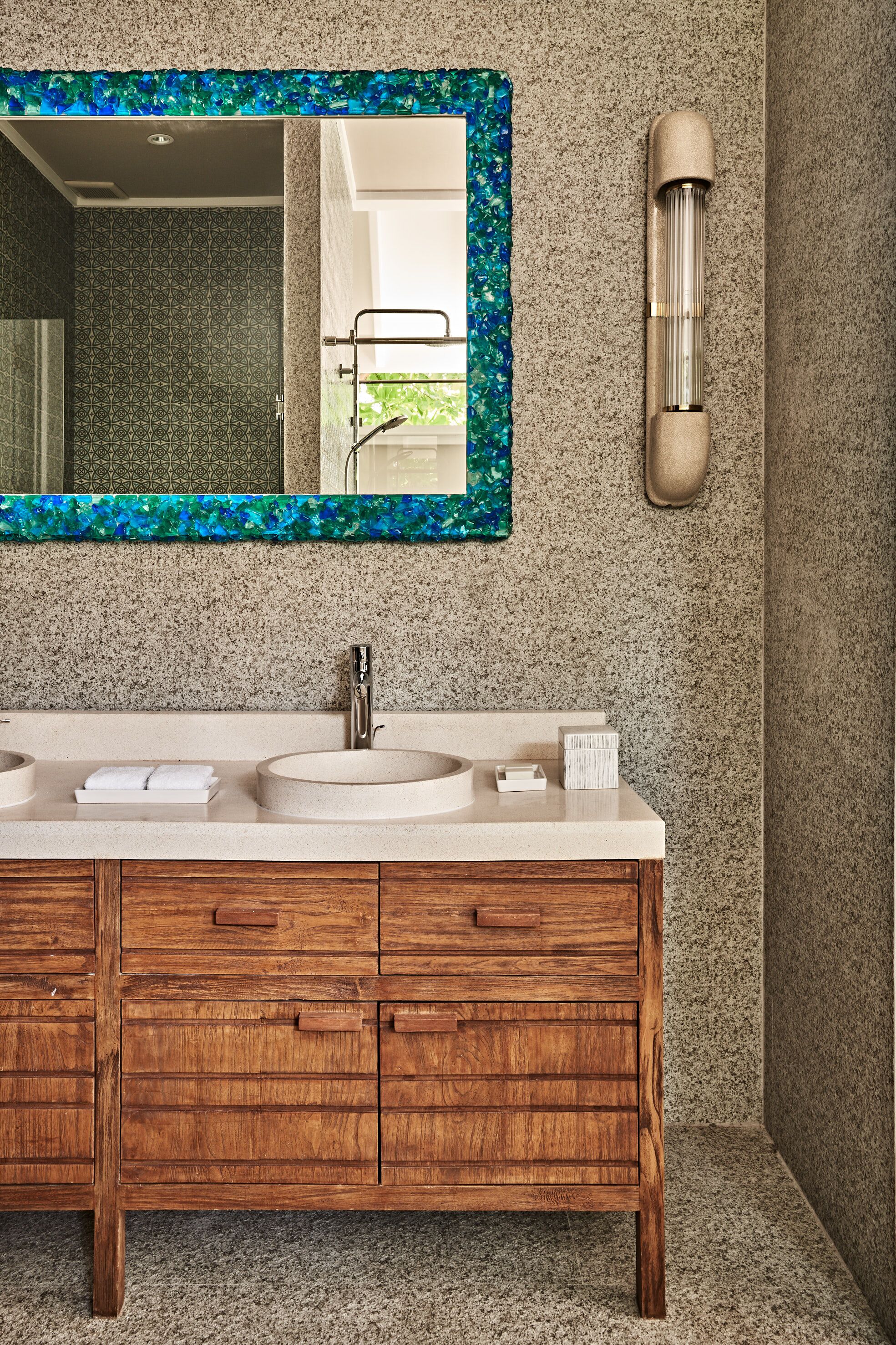 A bathroom with a granite countertop, two sinks, a wooden vanity, a mirror with a blue frame, and a towel rack.
