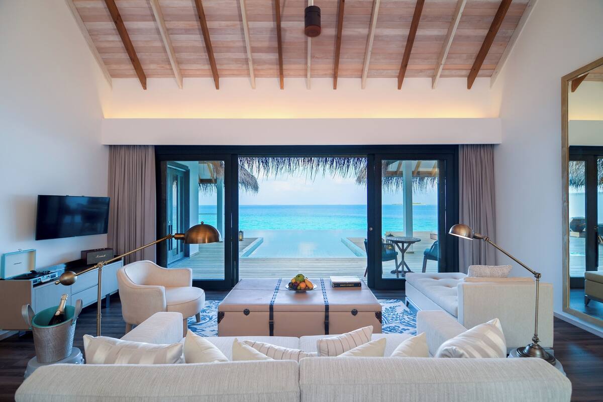 Une chambre d’hôtel moderne, dotée d’un grand lit, d’un canapé, d’une table basse et d’un téléviseur. La chambre offre une vue sur l’océan grâce à de grandes fenêtres.