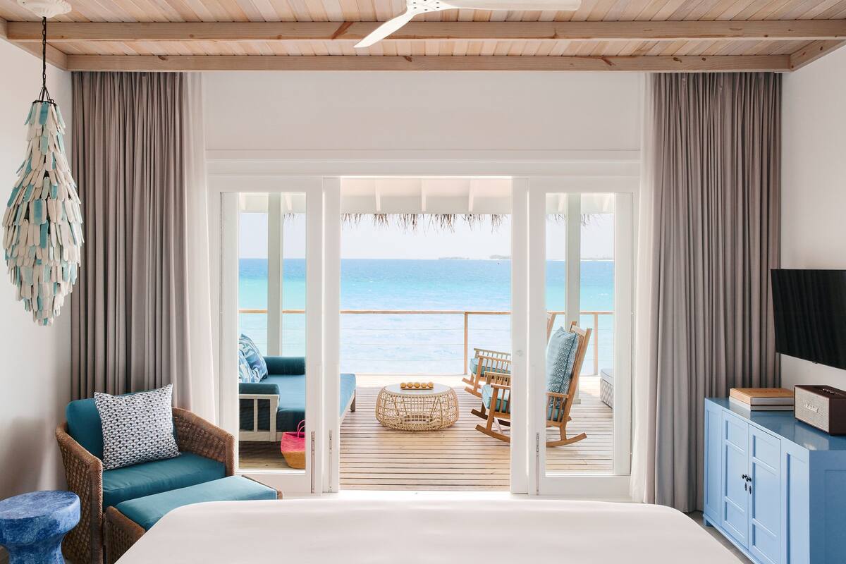 Une chambre avec un grand lit, une vue sur la mer, une terrasse en bois avec des meubles d’extérieur et un téléviseur posé sur un meuble.