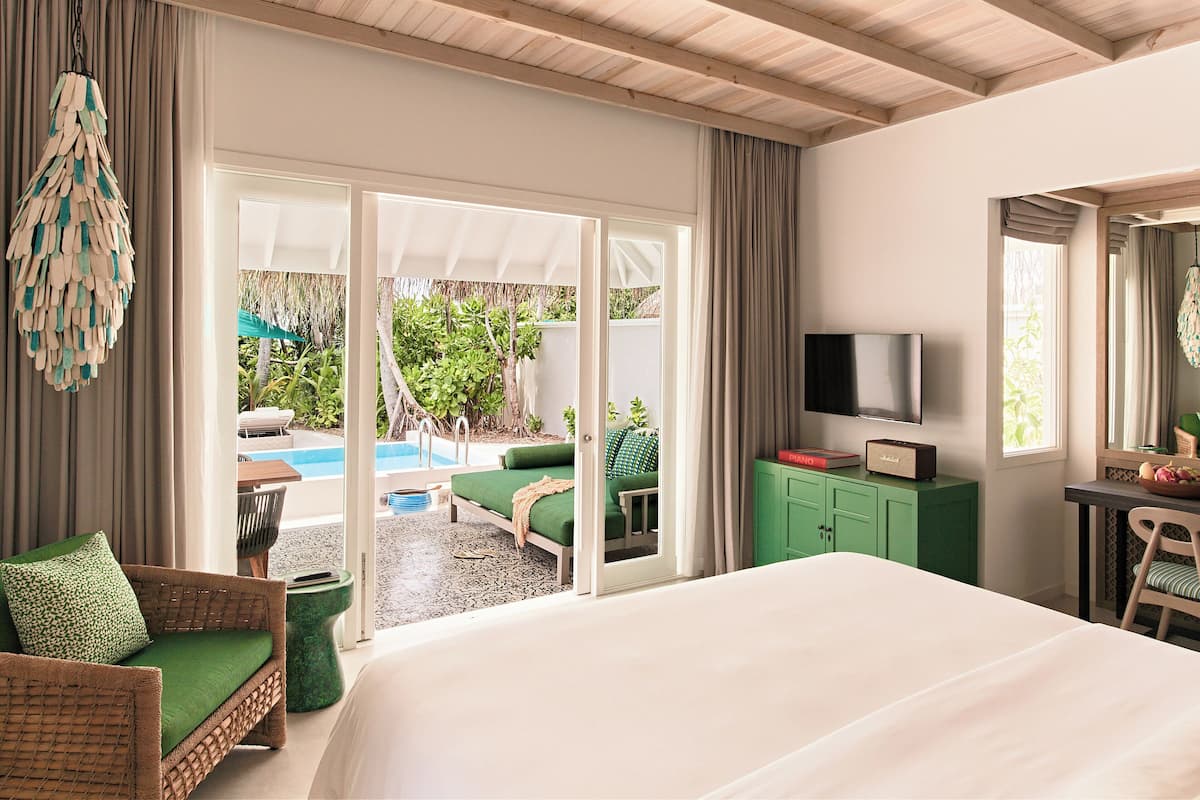 Une chambre d’hôtel dotée d’un grand lit, d’une télévision, d’un bureau avec une chaise et offrant une vue sur une piscine extérieure et un espace verdoyant.