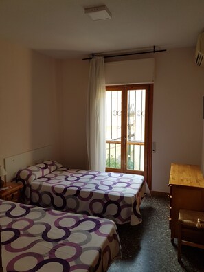 Una habitación con dos camas, un escritorio de madera y una ventana con vistas a la vegetación.