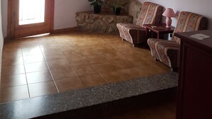 A room with a stone staircase, a wooden door with a sign, a red decorative item on the wall, and two patterned chairs with a small table and a lamp. - Hostal L Escaleta (Oropesa del Mar)