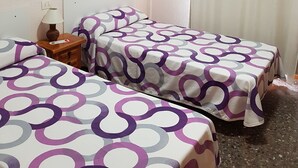 A hotel room with two beds, a wooden nightstand with a lamp, and a window with curtains. - Hostal L Escaleta (Oropesa del Mar)