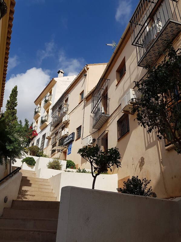 Una hilera de edificios de varios pisos con balcones, una escalera que lleva a la entrada y un letrero que indica un albergue.
