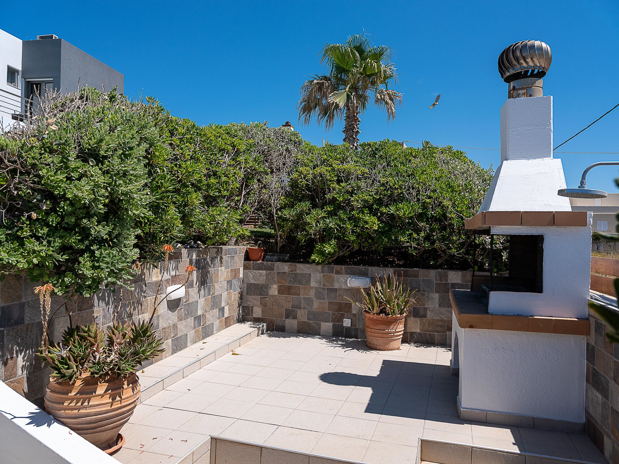 Un patio con plantas en macetas, un muro de piedra y una chimenea blanca.