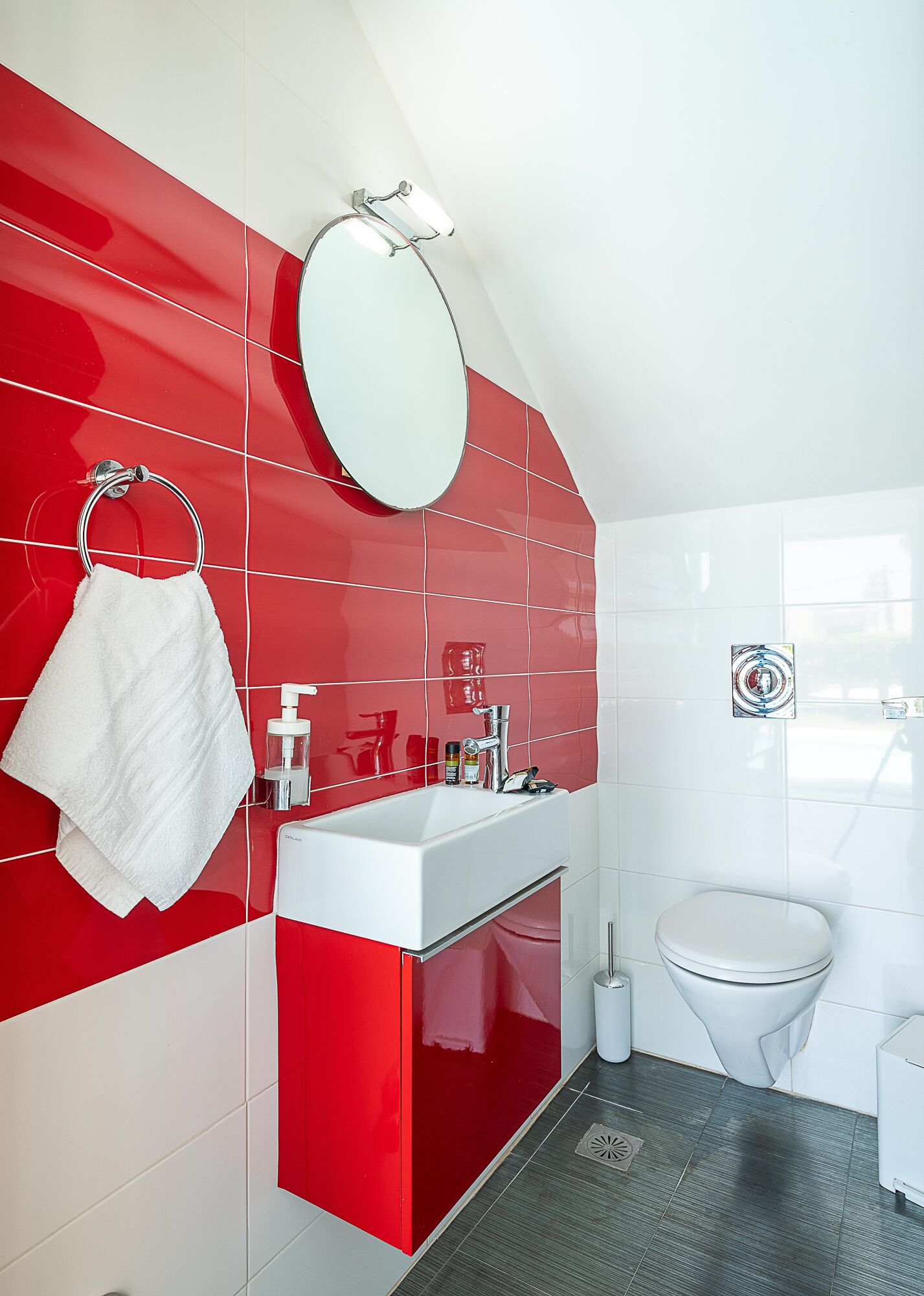 Un baño moderno con baldosas rojas y blancas, un lavamanos blanco, un espejo y un inodoro.