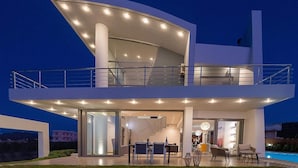 Una casa moderna de dos pisos con techo plano, ventanas amplias y un balcón.