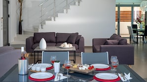 Un comedor moderno con una mesa de vidrio dispuesta para cuatro personas, un sofá y una escalera al fondo.