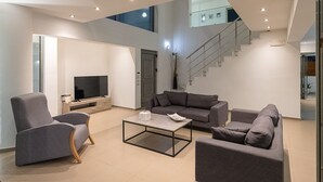 Una sala de estar moderna con un televisor de pantalla plana, sofás grises, una mesa de centro y una escalera que sube a un nivel superior.