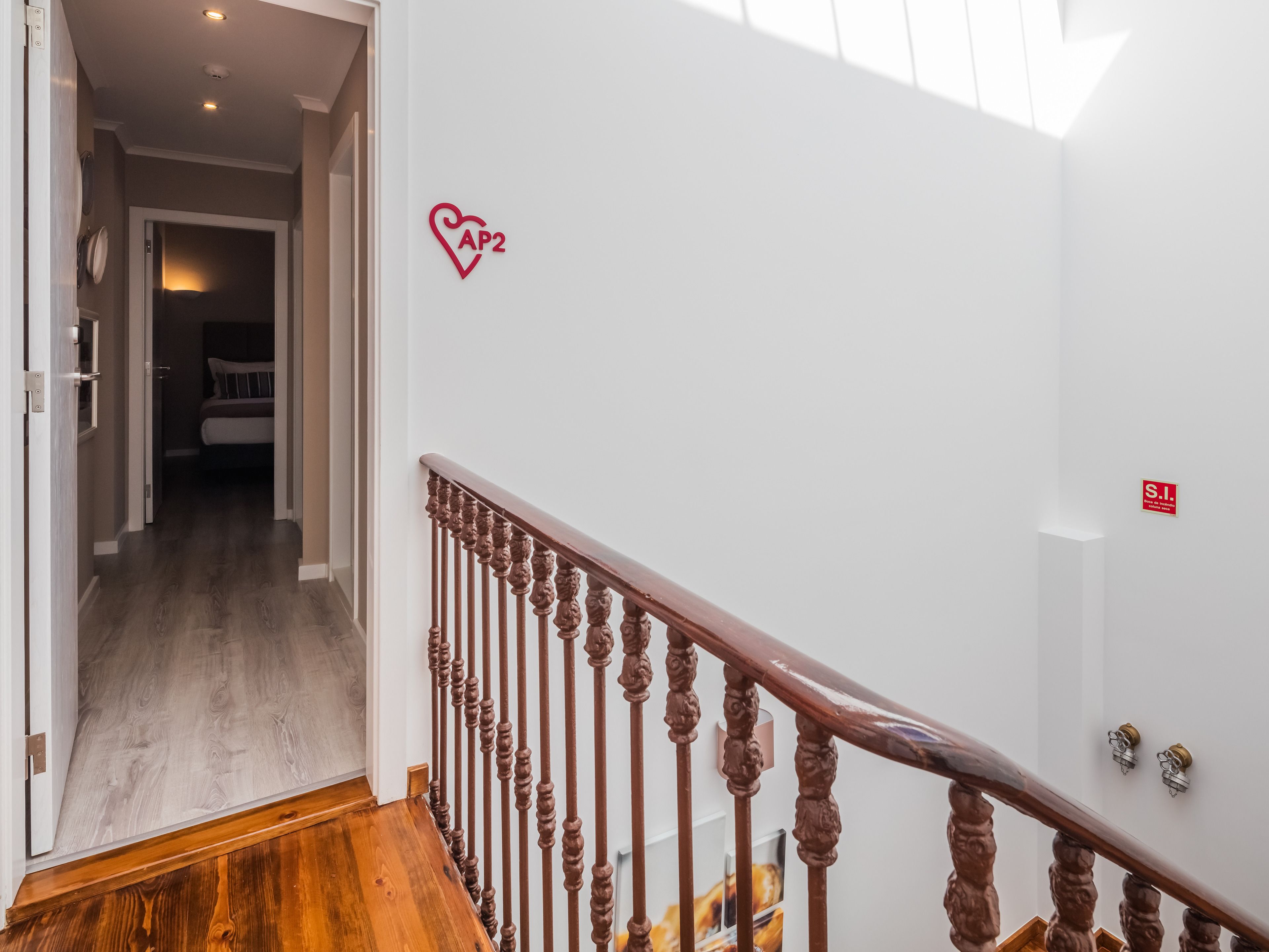 A staircase with a wooden handrail leading to a bedroom with a bed and a nightstand.