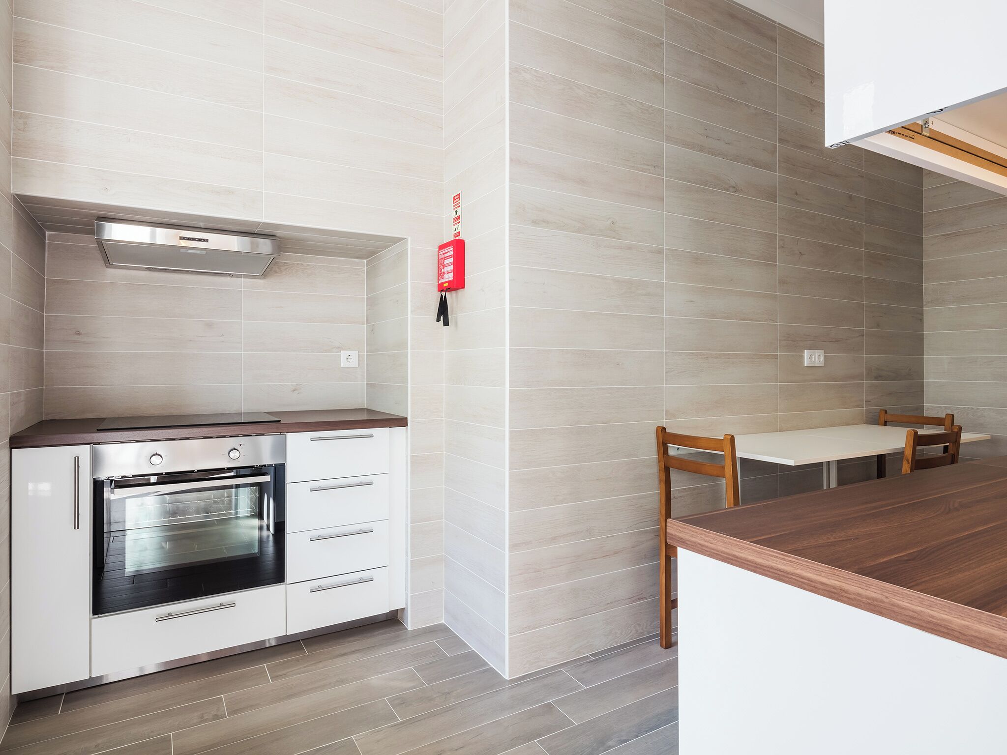 Una cocina moderna con horno empotrado, armarios blancos y una mesa de comedor de madera.