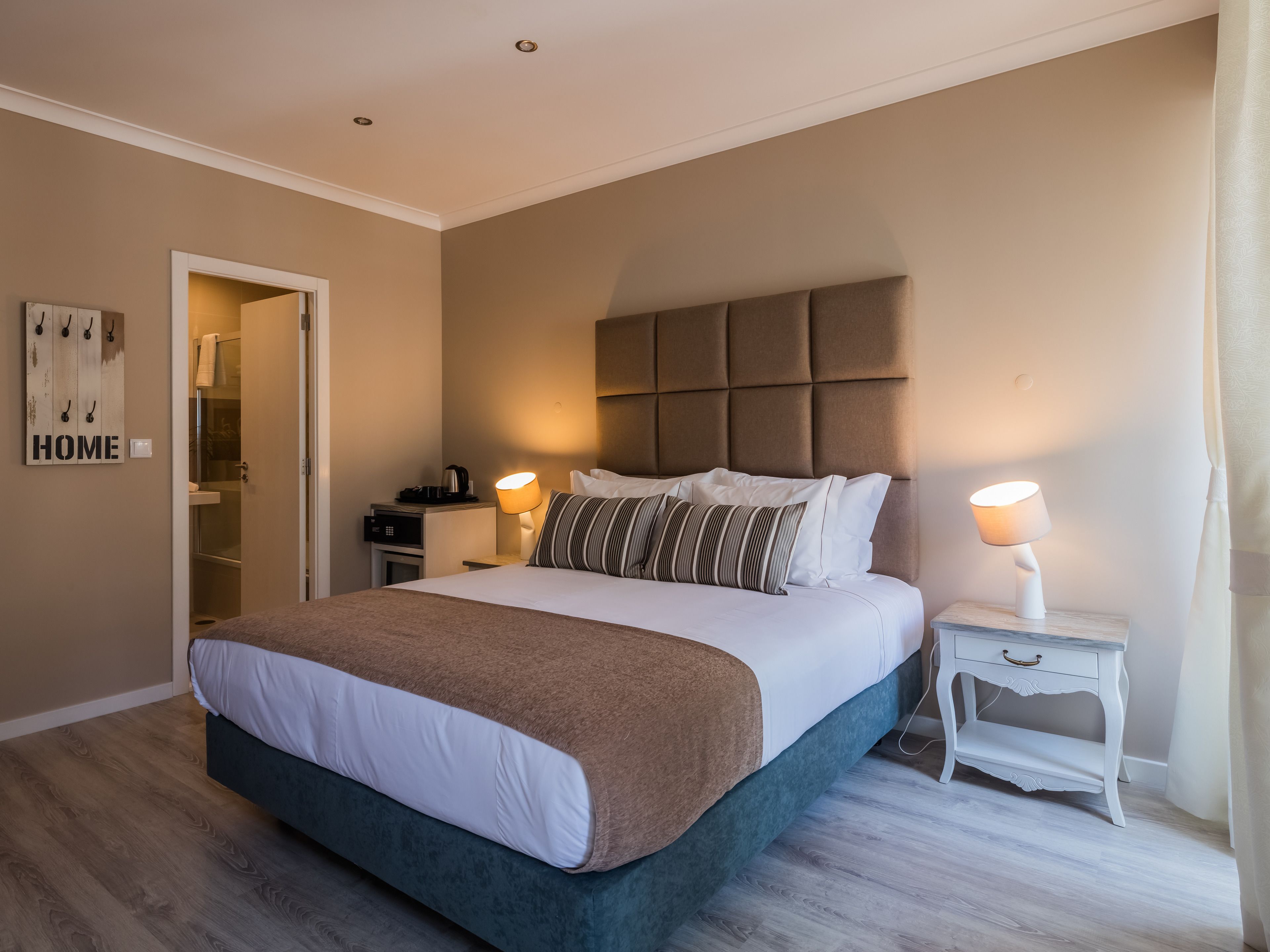 Un dormitorio con una cama grande, mesitas de noche, una lámpara de pared y una puerta que da al baño.