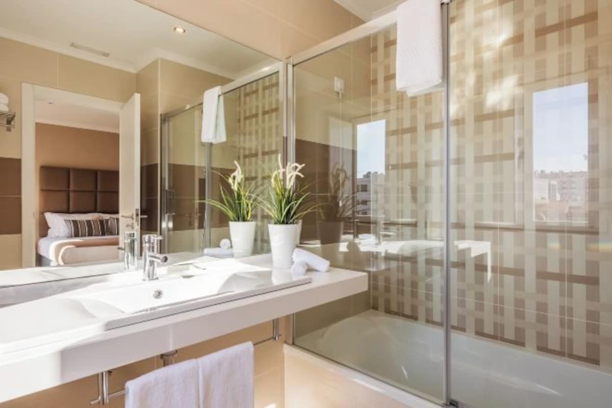 A modern bathroom with a large mirror, a shower enclosure, and a view of the city.