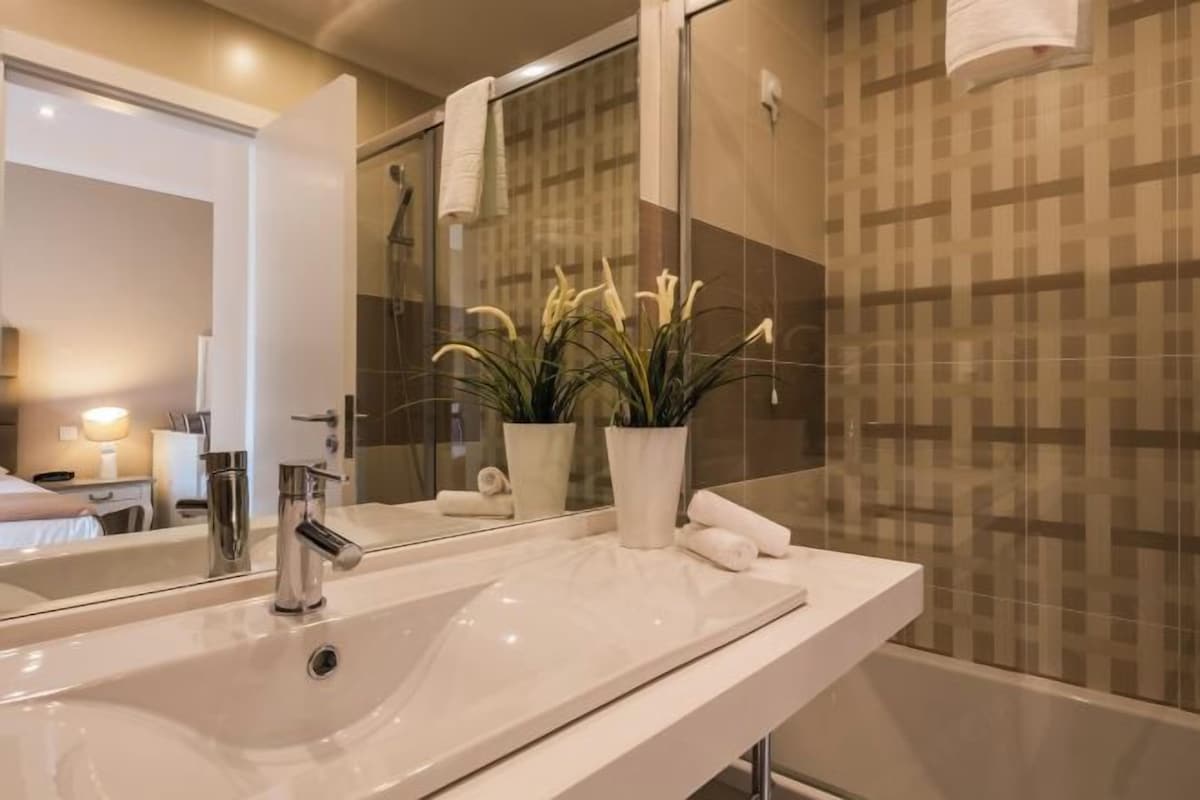 A bathroom with a large mirror, a sink, a shower, and a potted plant.