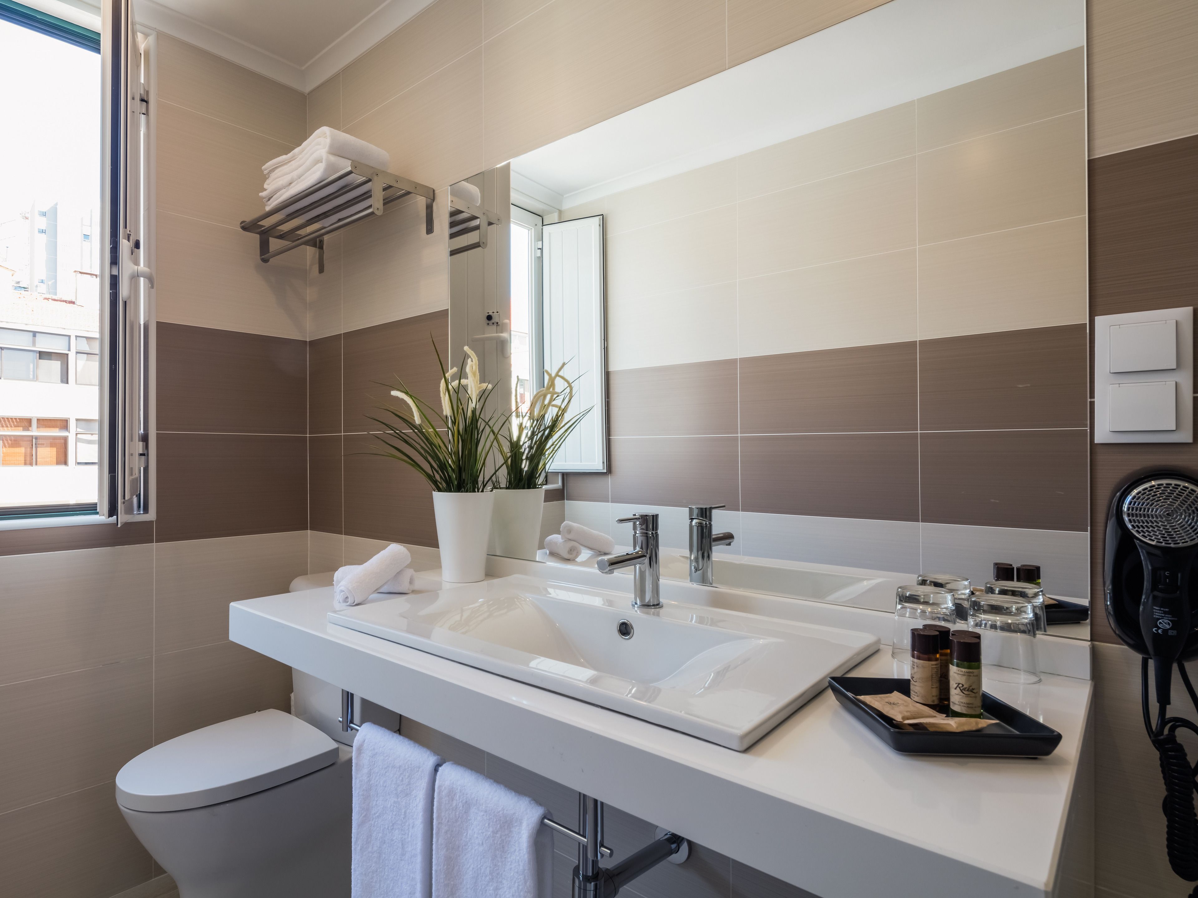 Un bagno moderno con un lavandino bianco, due portasci da asciugamano, una pianta in vaso e un asciugacapelli sul ripiano.