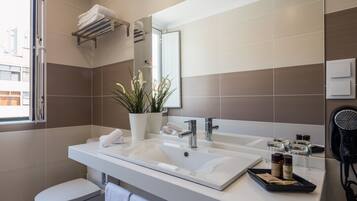Ein modernes Badezimmer mit einem weißen Waschbecken, zwei Handtuchhaltern, einer Topfpflanze und einem Fön auf der Ablagefläche.