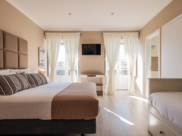 A bedroom with a bed, a desk, a TV, and a balcony. - Vila Garden Guesthouse (Lisbon)
