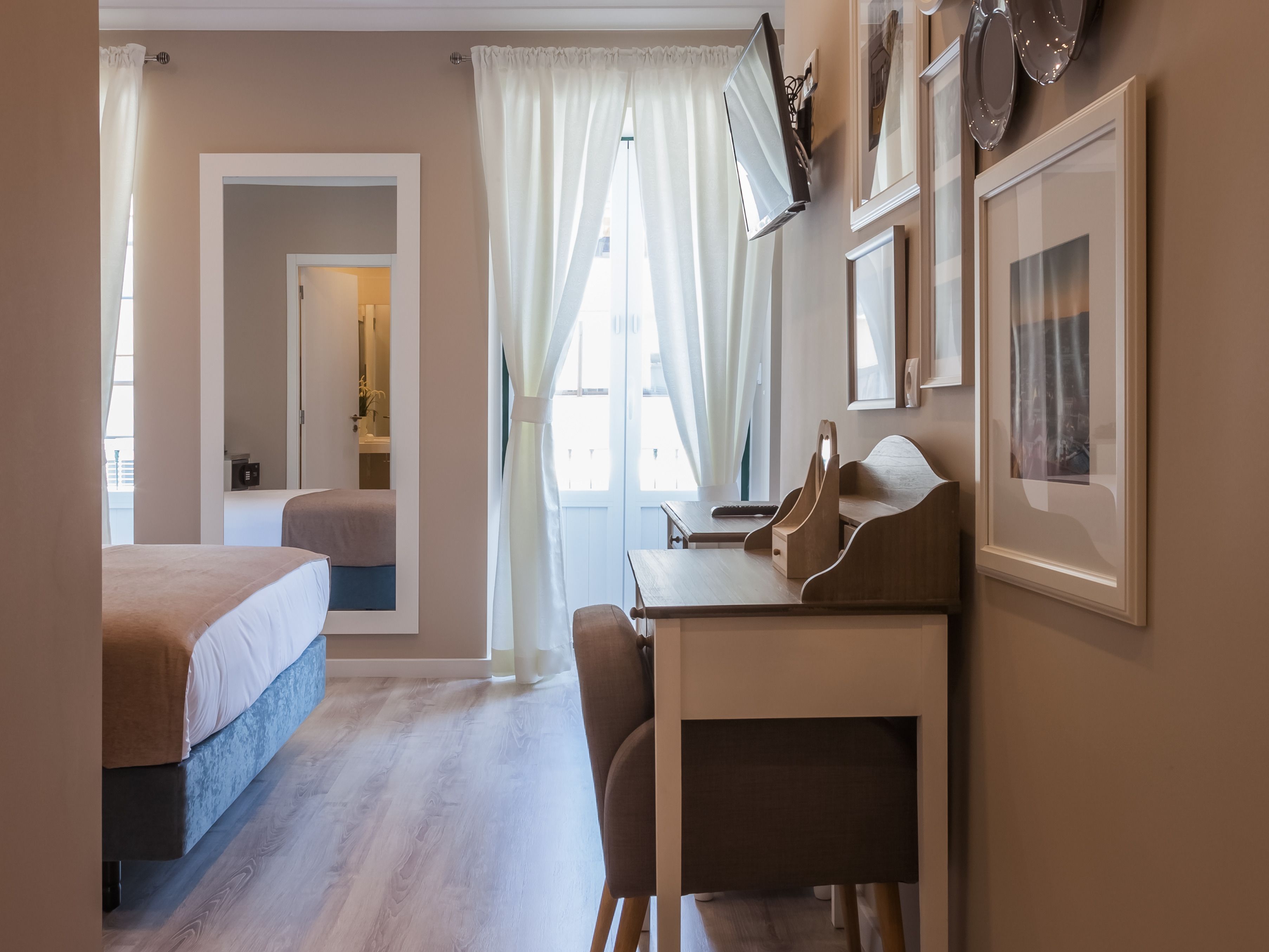 Ett hotellrum med en säng, ett skrivbord, en stol, en tv och ett fönster med gardiner.