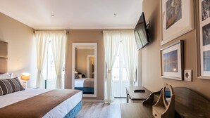 Ein Hotelzimmer mit einem großen Bett, einem Schreibtisch, einem Sessel und einem Fernseher an der Wand.