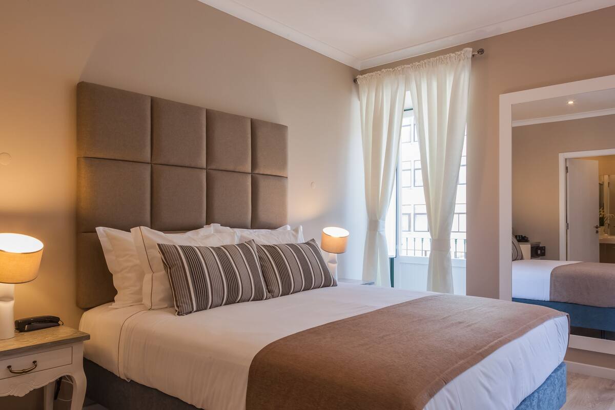 A hotel room with a large bed, two bedside lamps, a nightstand, and a window with curtains.