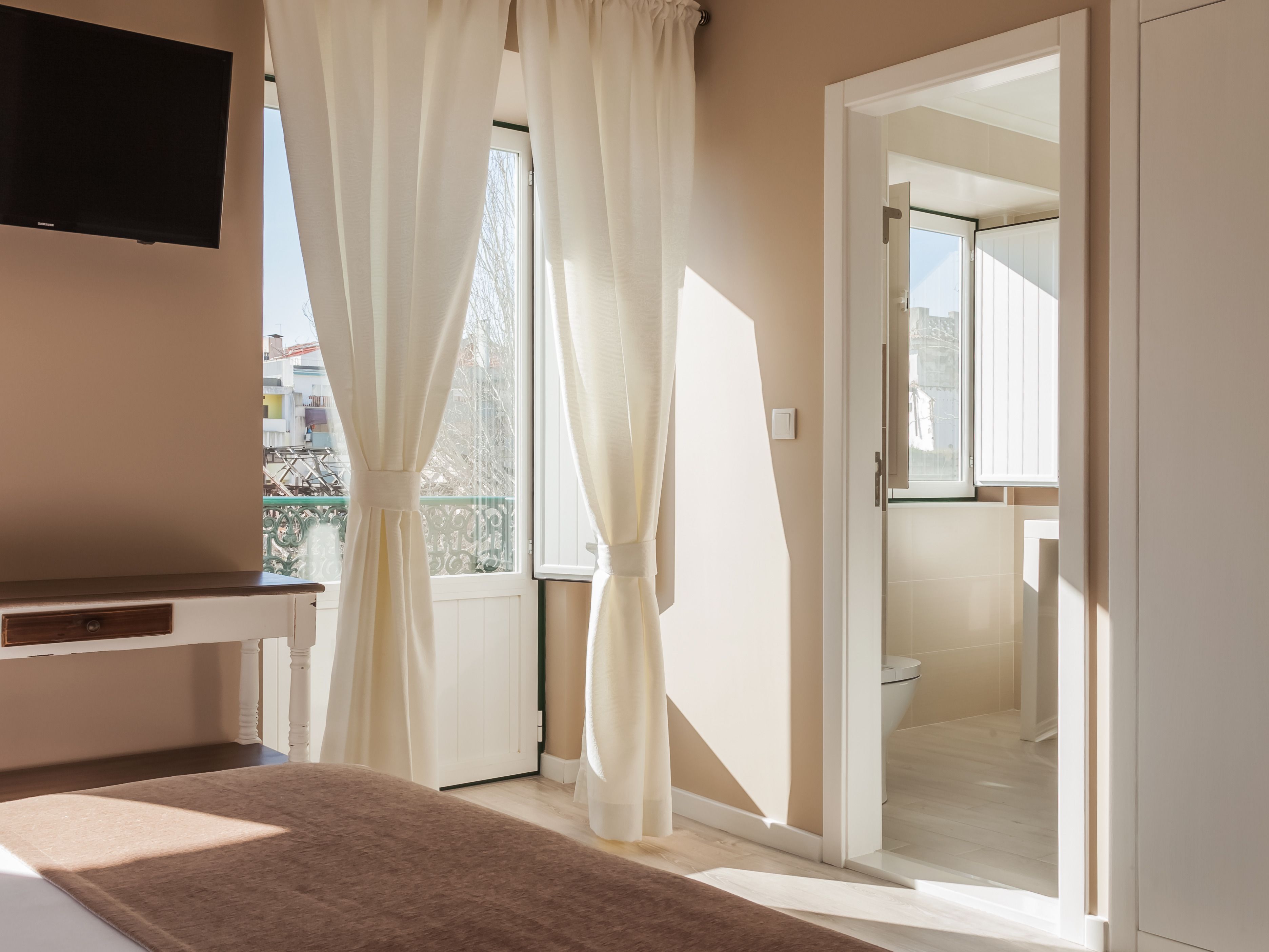 A hotel room with a bed, a TV, a window with curtains, and a bathroom visible through an open door.