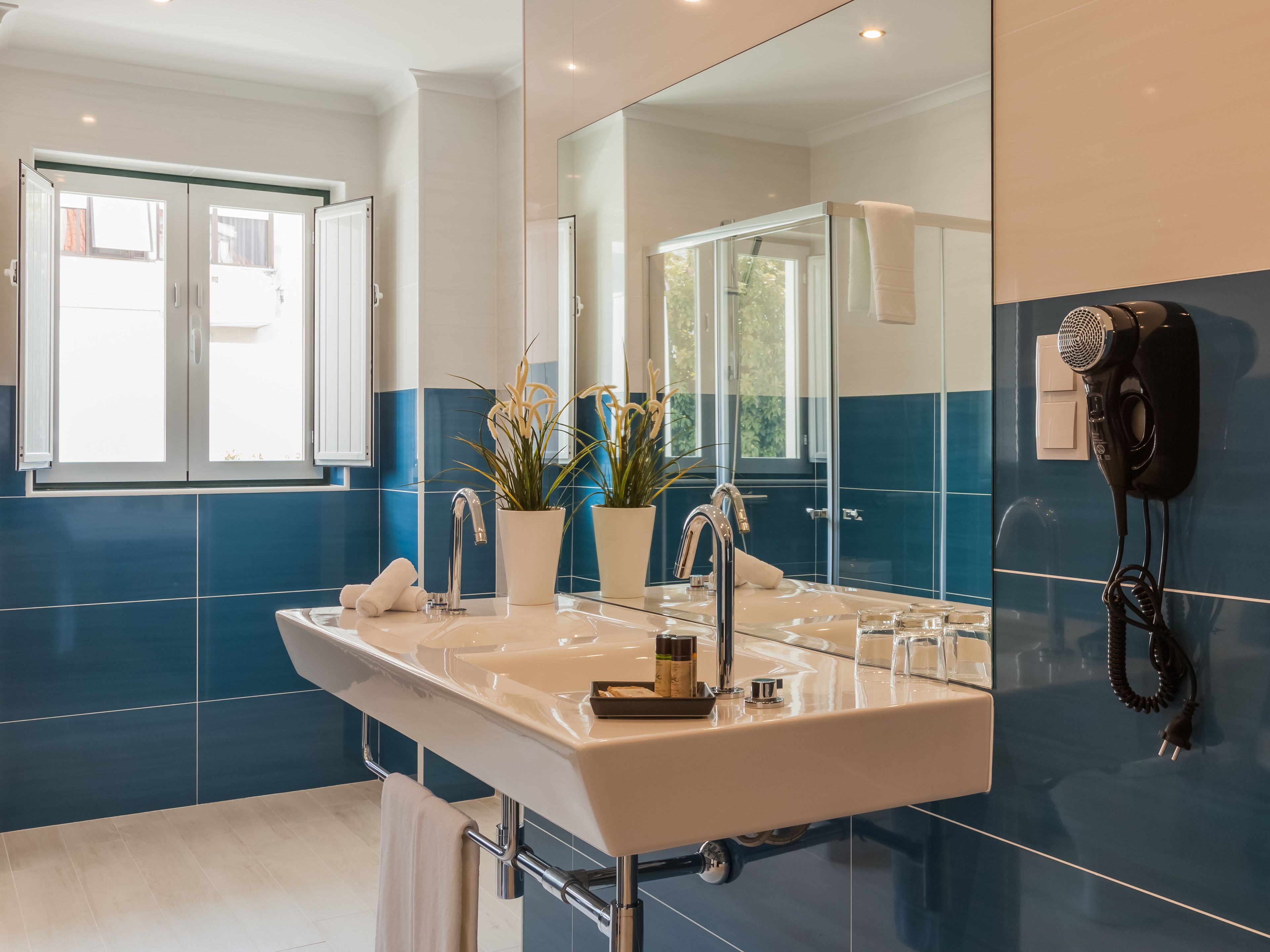 Un baño moderno con un espejo grande, lavamanos dobles y un secador de pelo montado en la pared.