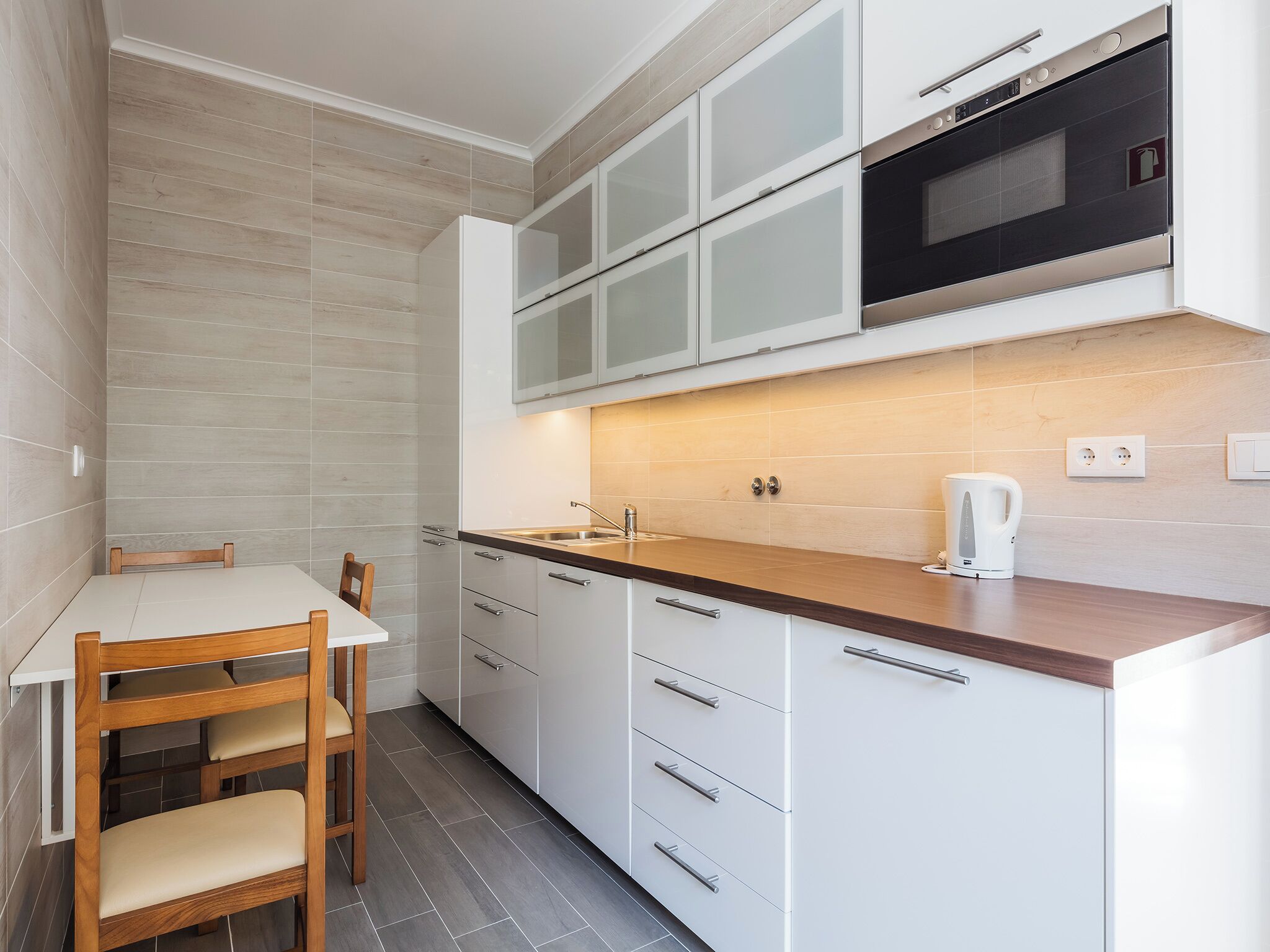 A compact kitchen with white cabinets, a wooden countertop, a built-in oven, and a kettle.