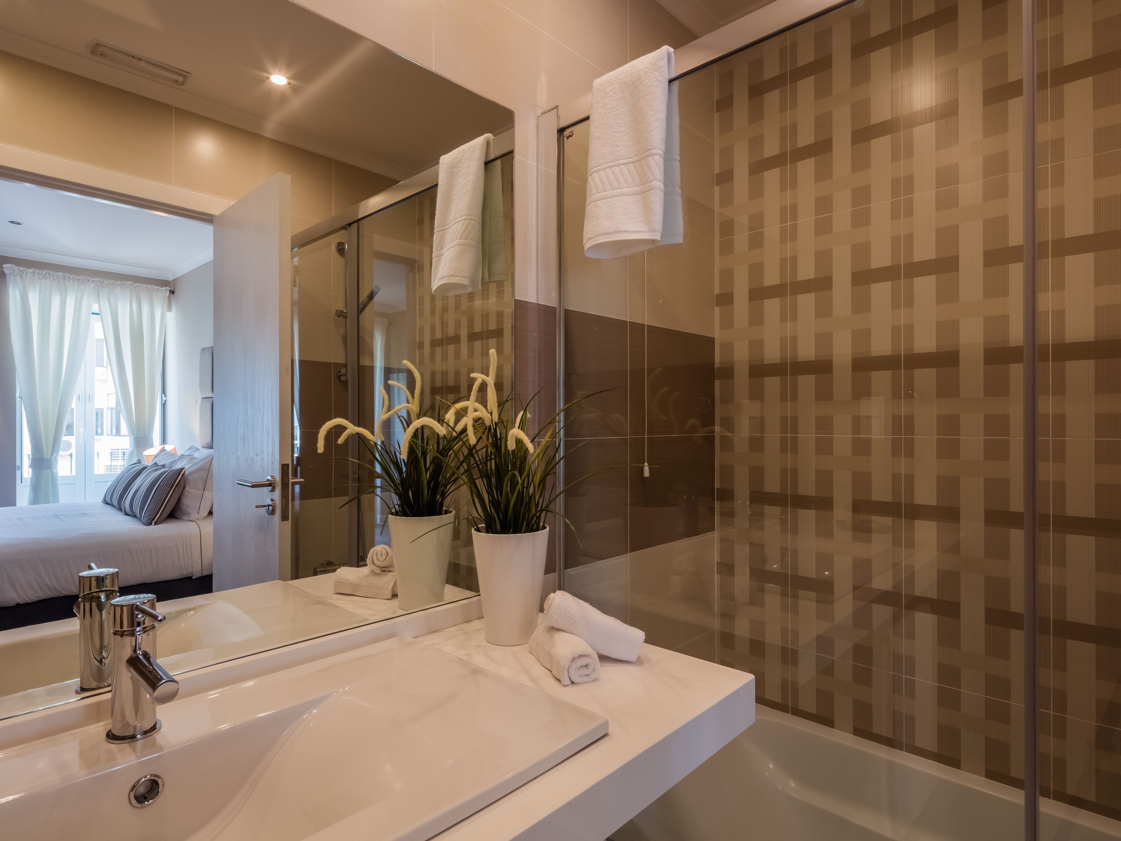 Een moderne badkamer met een grote spiegel, een wit wastafelmeubel en een douchecabine van glas.