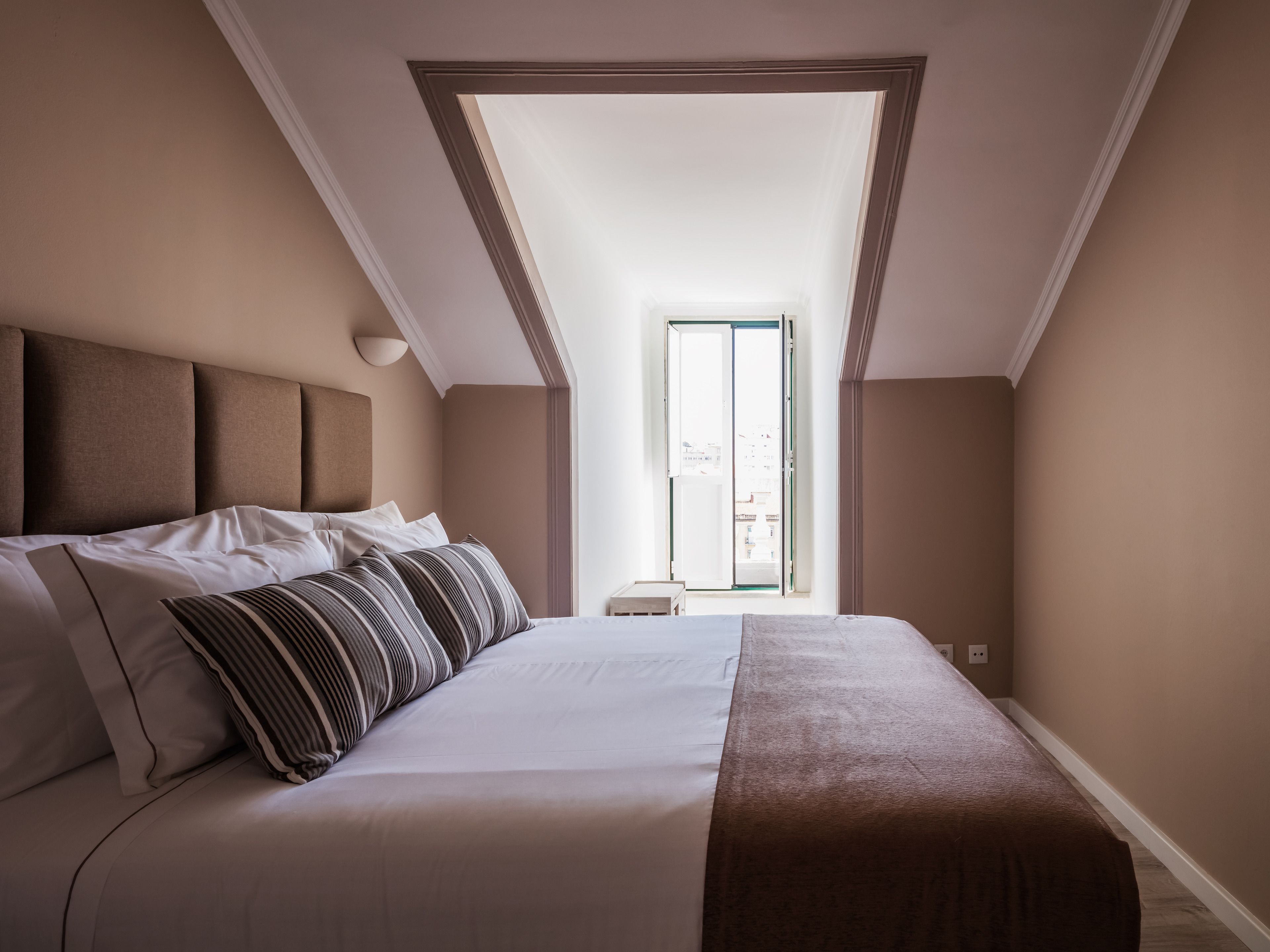 A bedroom with a large bed, a view of the city through a window, and a door leading to an outdoor area.