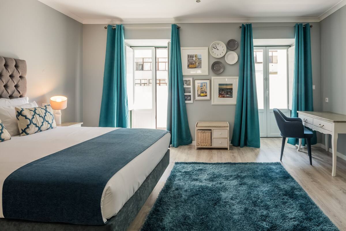 A modern bedroom with a bed, desk, and a view through the window.