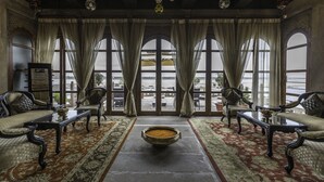 A room with a large window, a sofa, a table, and a decorative bowl. - BrijRama Palace, Varanasi - By the Ganges (Varanasi)