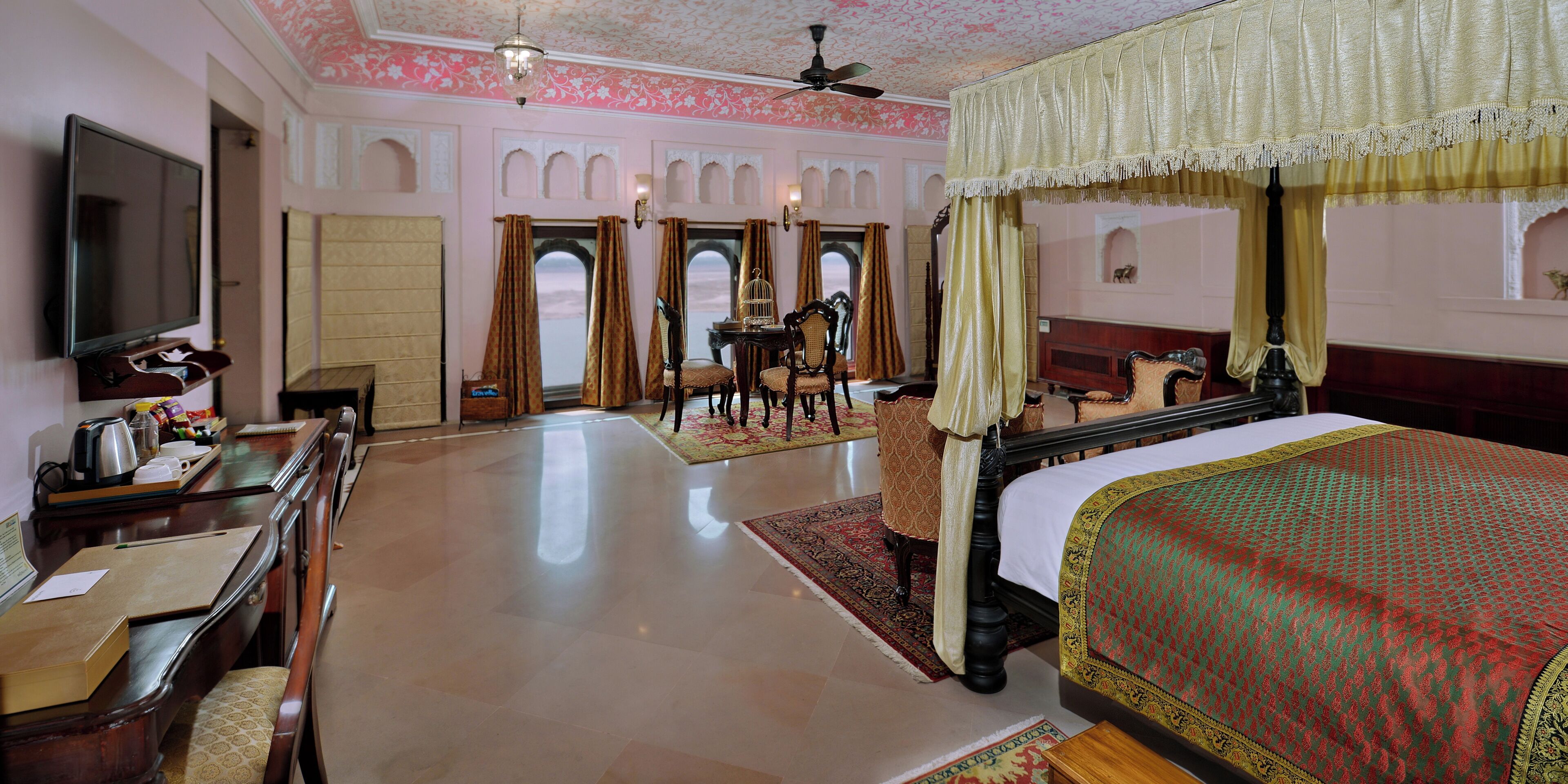 Une chambre d’hôtel dotée d’un grand lit, d’un bureau avec un téléviseur à écran plat, d’un coin repas avec des chaises et d’une vue sur l’extérieur grâce à des fenêtres en arc de cercle.