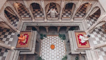 A courtyard with a checkered floor, ornate columns, and two individuals seated on red carpets.