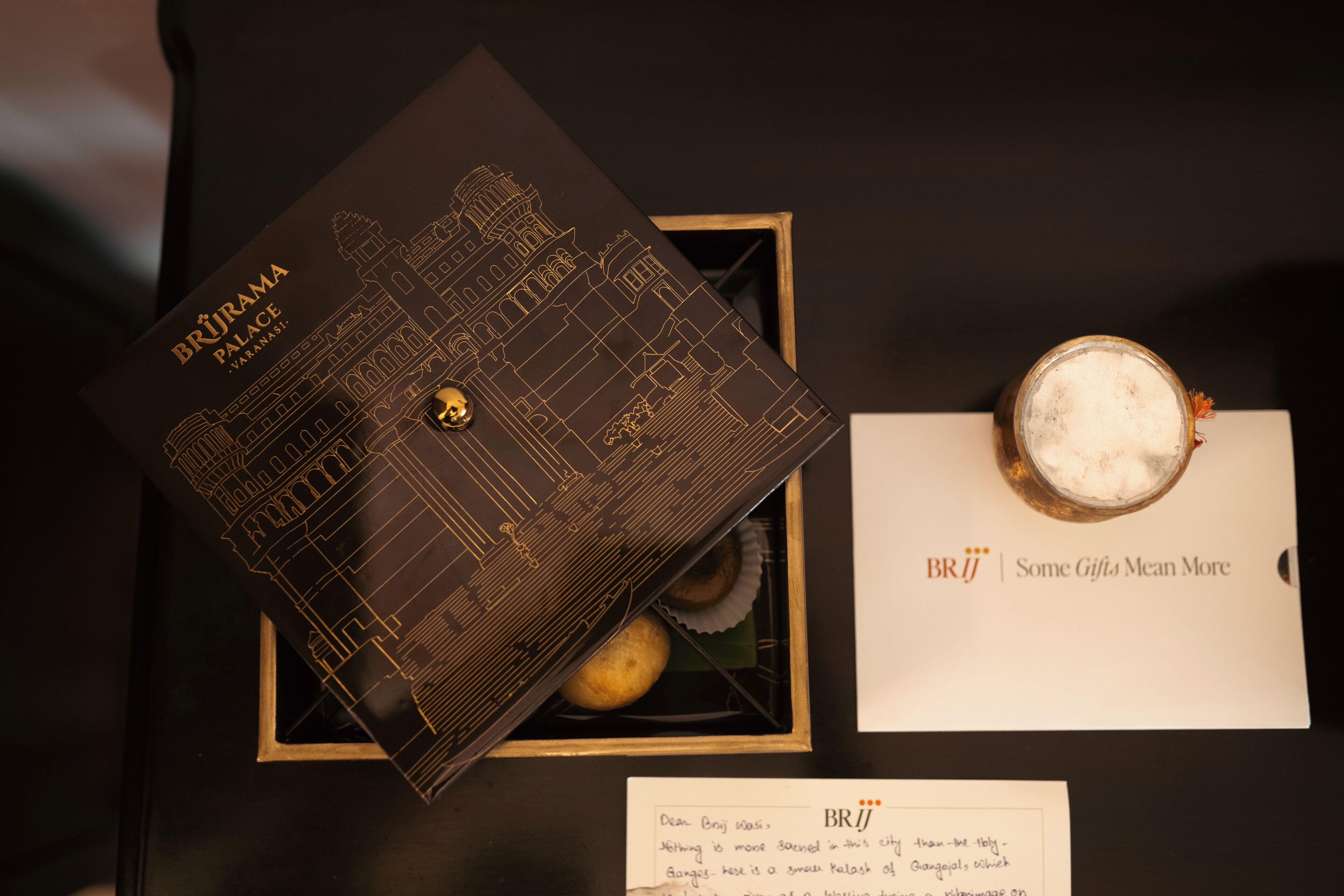 A Brûroma Palace branded box with a detailed design, a glass of a creamy beverage, and a card with the text 'BRIJ | Some Gifts Mean More'.