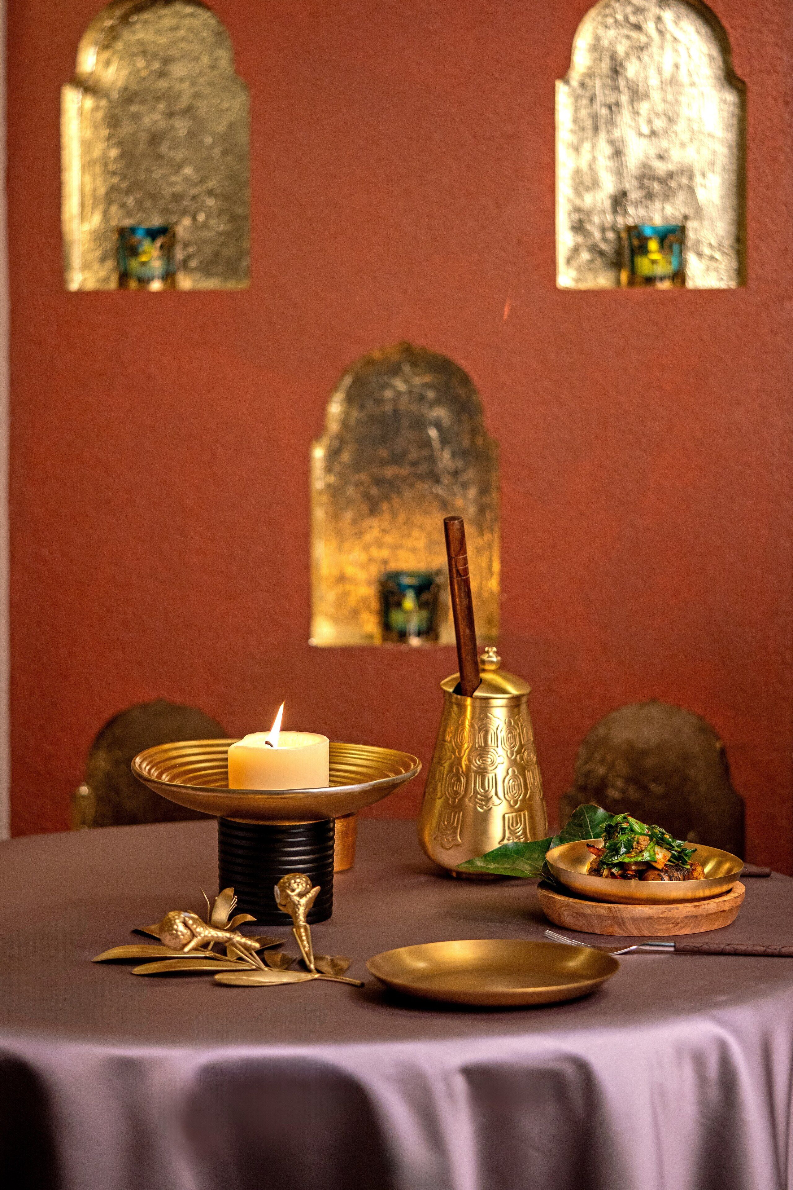 A table with a lit candle, a brass pitcher, and a plate of food.