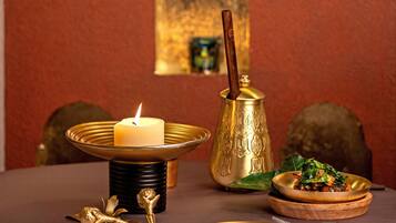 A table with a lit candle, a brass pitcher, and a plate of food.