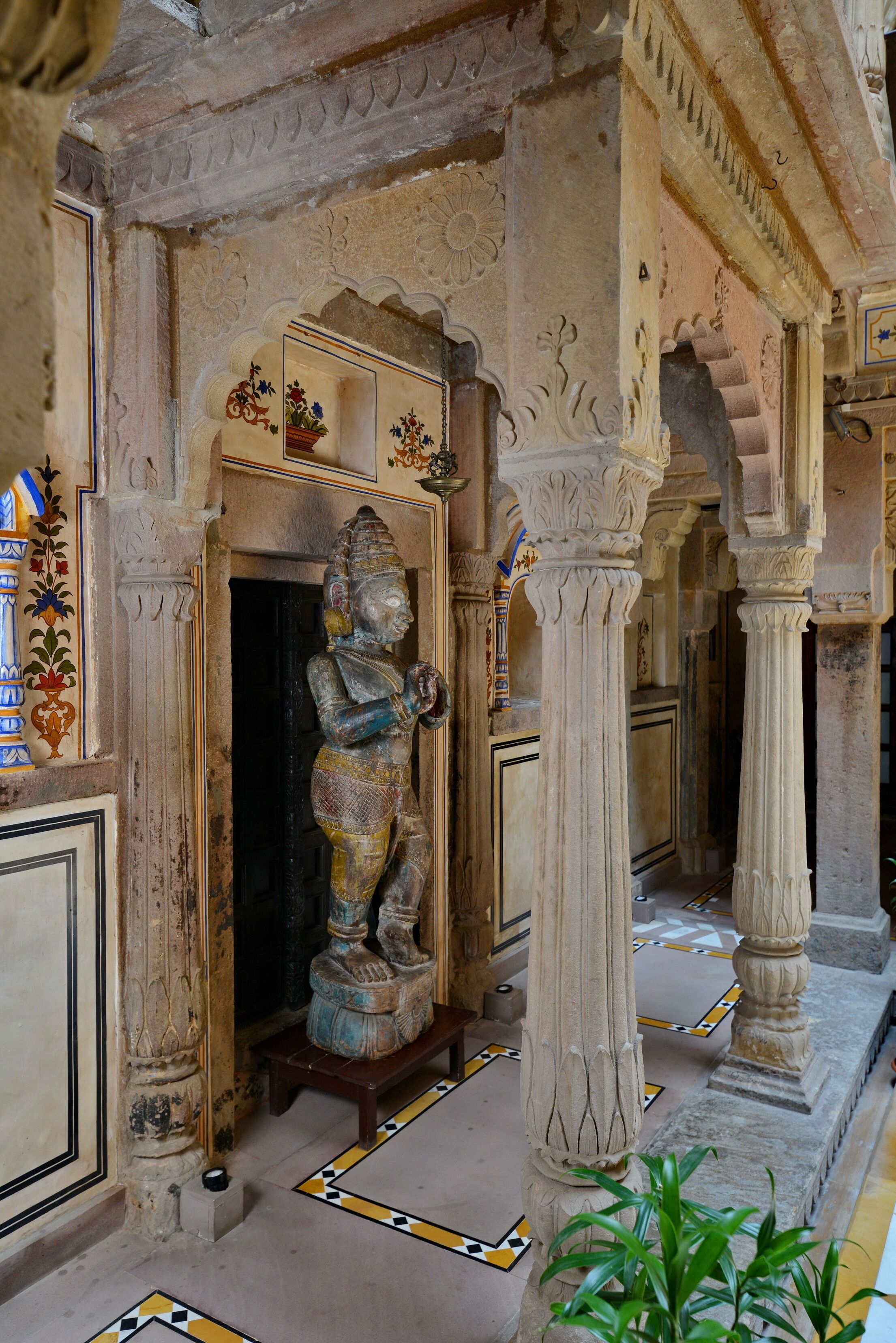 Un pasillo con columnas ornamentales, una estatua y un suelo de baldosas.