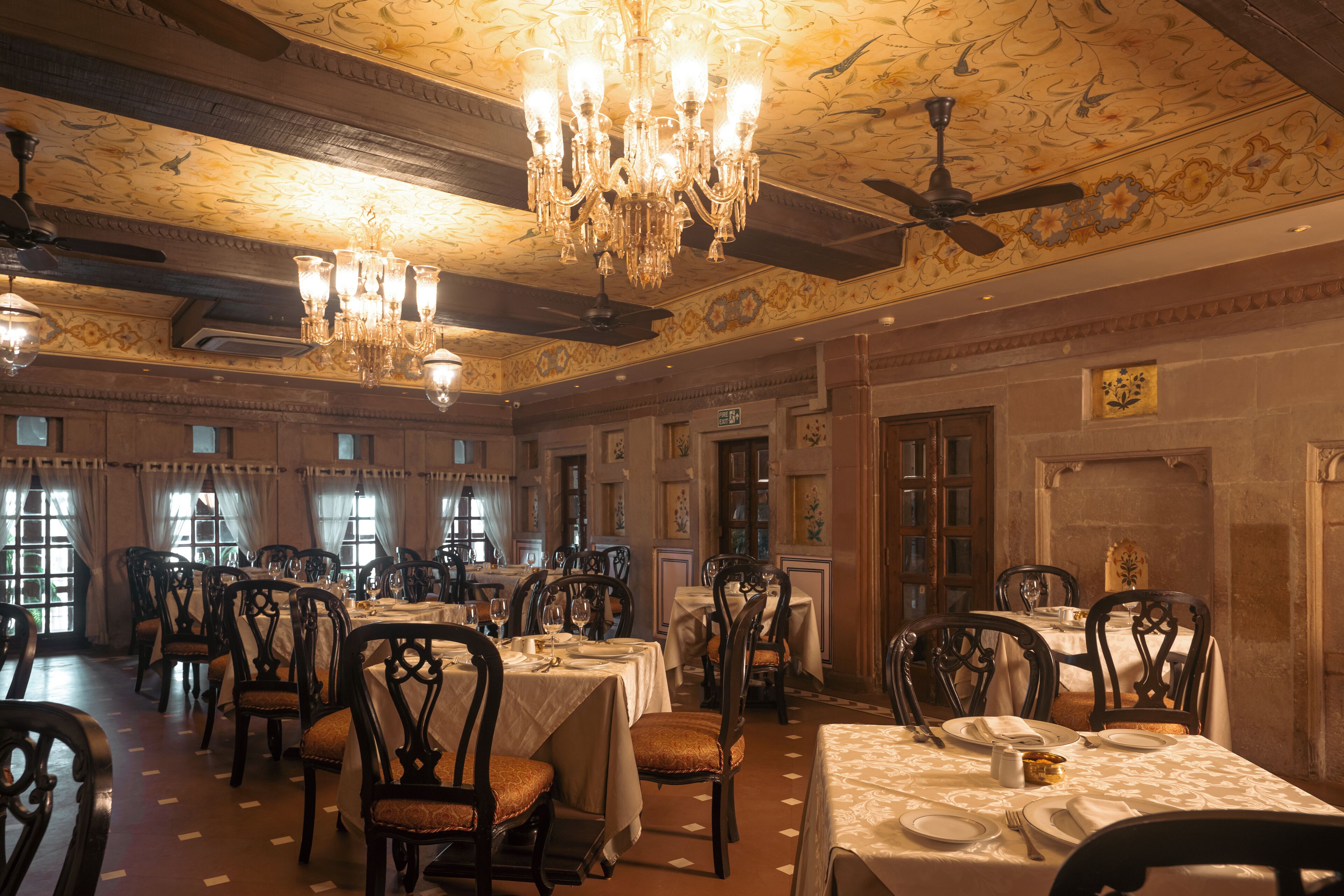 A dining area with multiple tables and chairs, chandeliers, and ceiling fans.