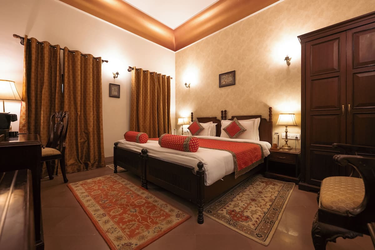 A hotel room with a bed, two bedside tables, a nightstand, a chair, and a desk with a lamp.