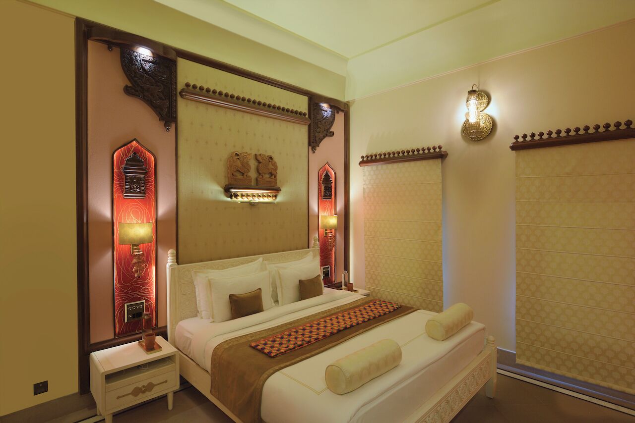 A hotel room with a large bed, a nightstand, a wall-mounted lamp, and a decorative headboard.