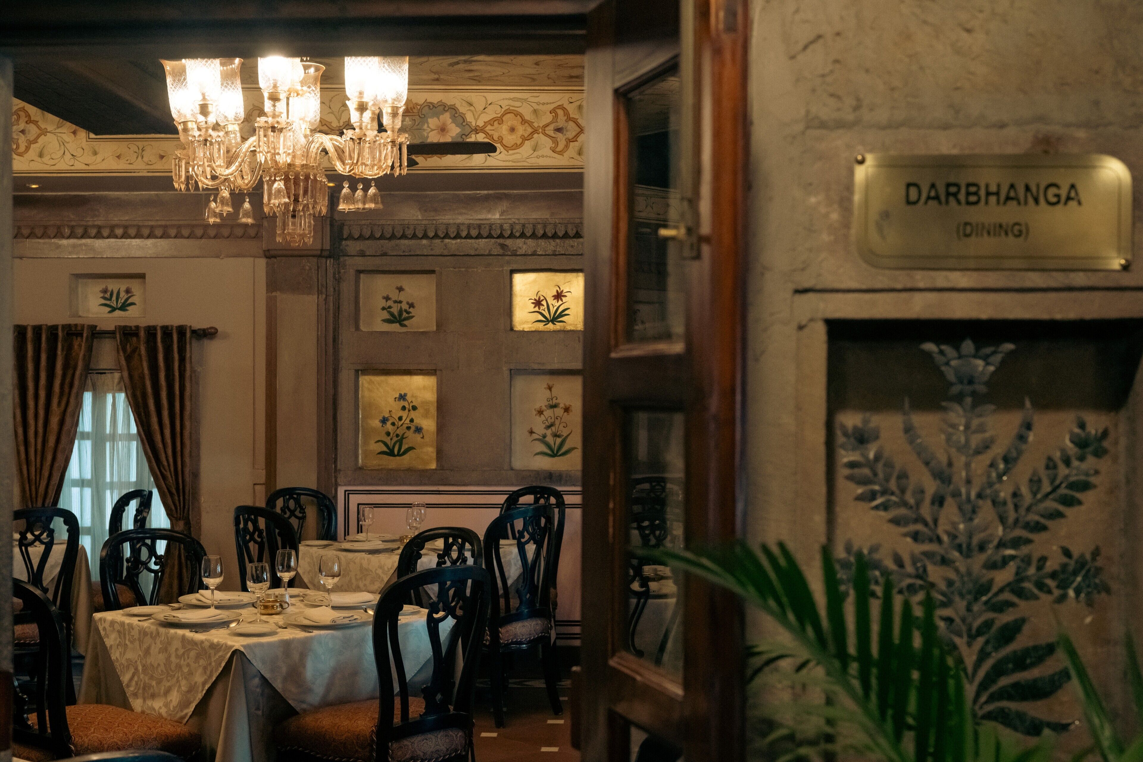 Comedor con candelabro, mesas, sillas y un cartel que indica 'DARBHANGA (DINING)'.