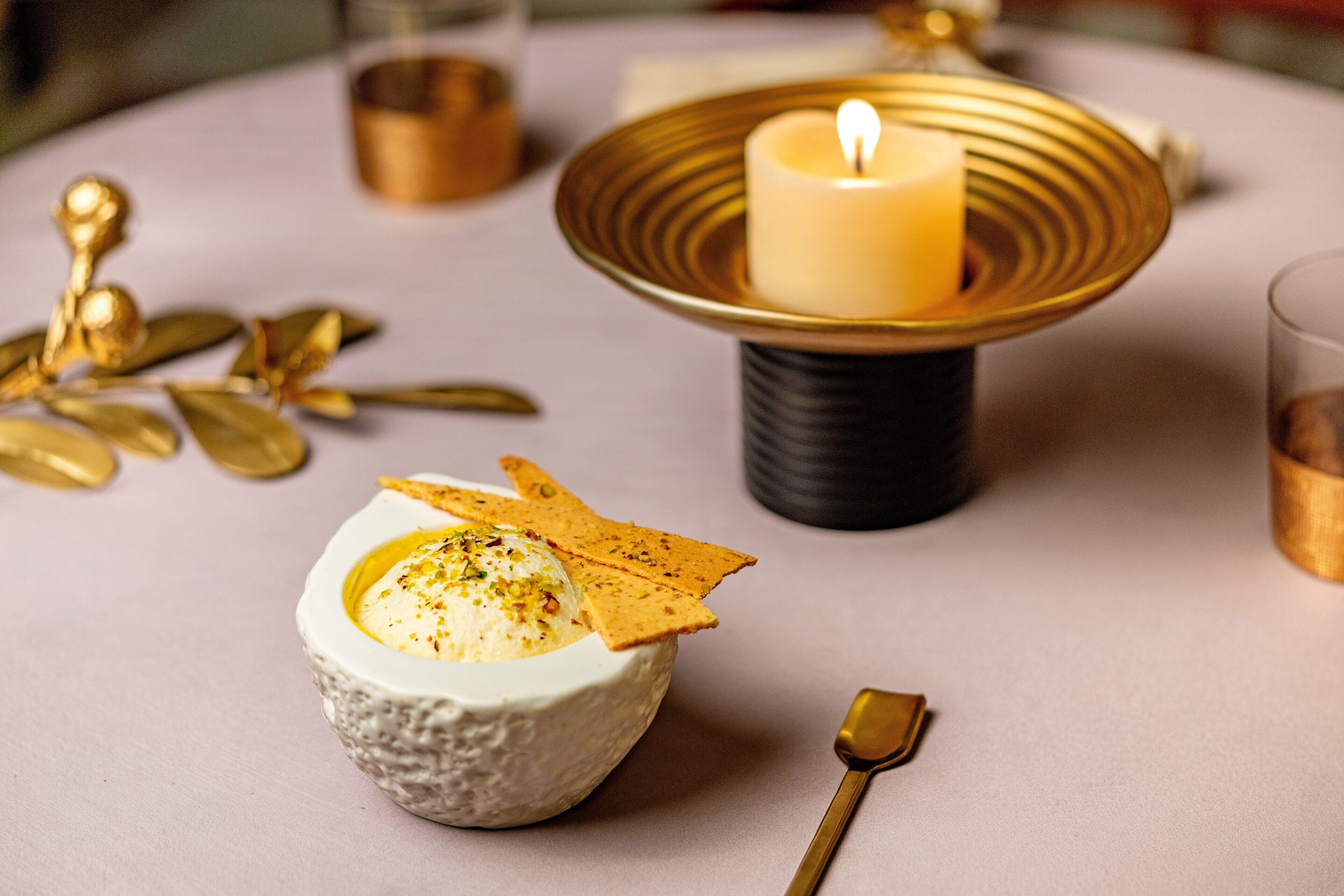 A dessert presentation on a table with a candle, gold decorative elements, and a spoon.