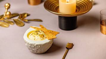 A dessert presentation on a table with a candle, gold decorative elements, and a spoon.
