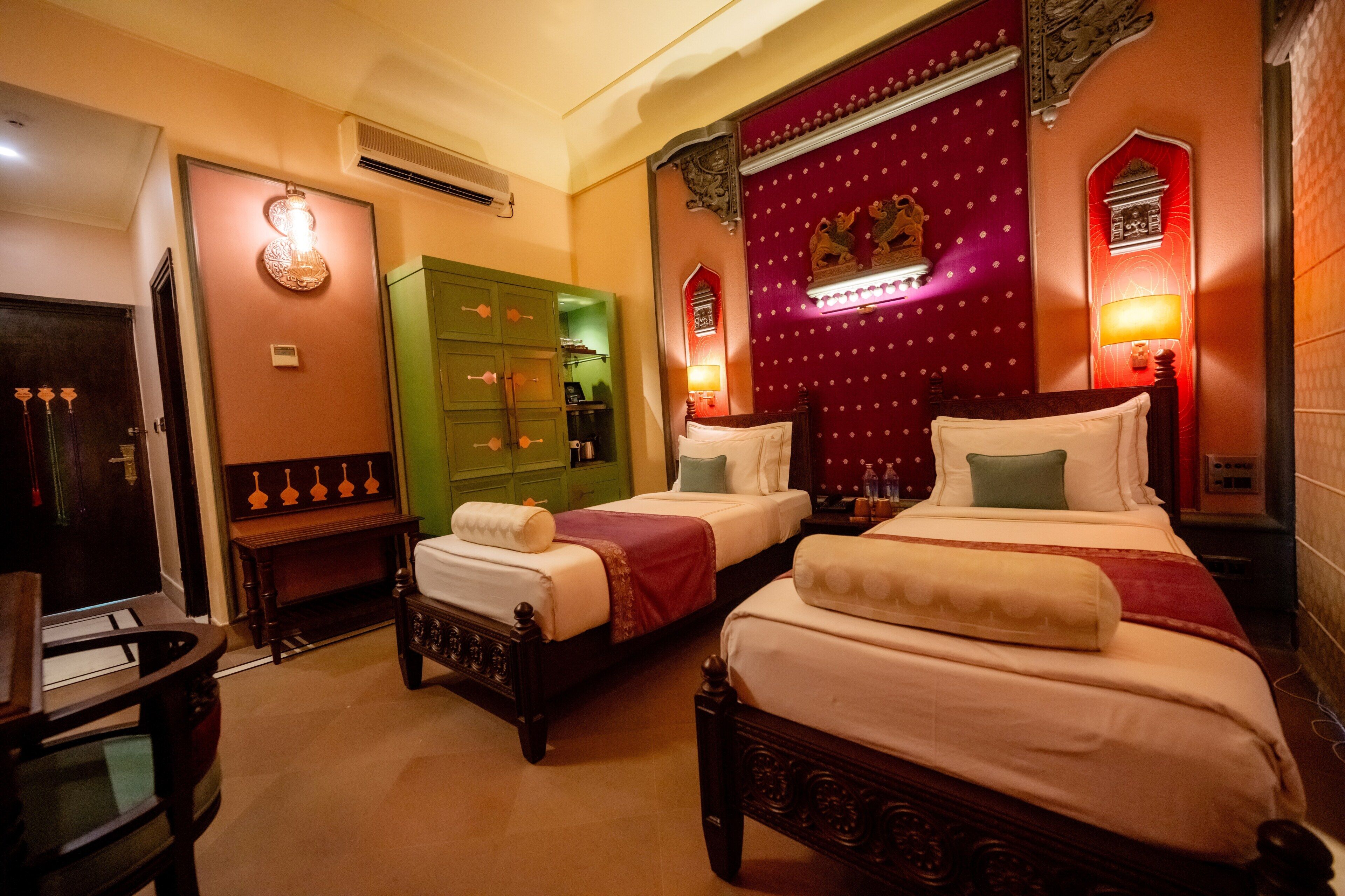 Habitación de hotel con dos camas, un armario verde y apliques decorativos en la pared.