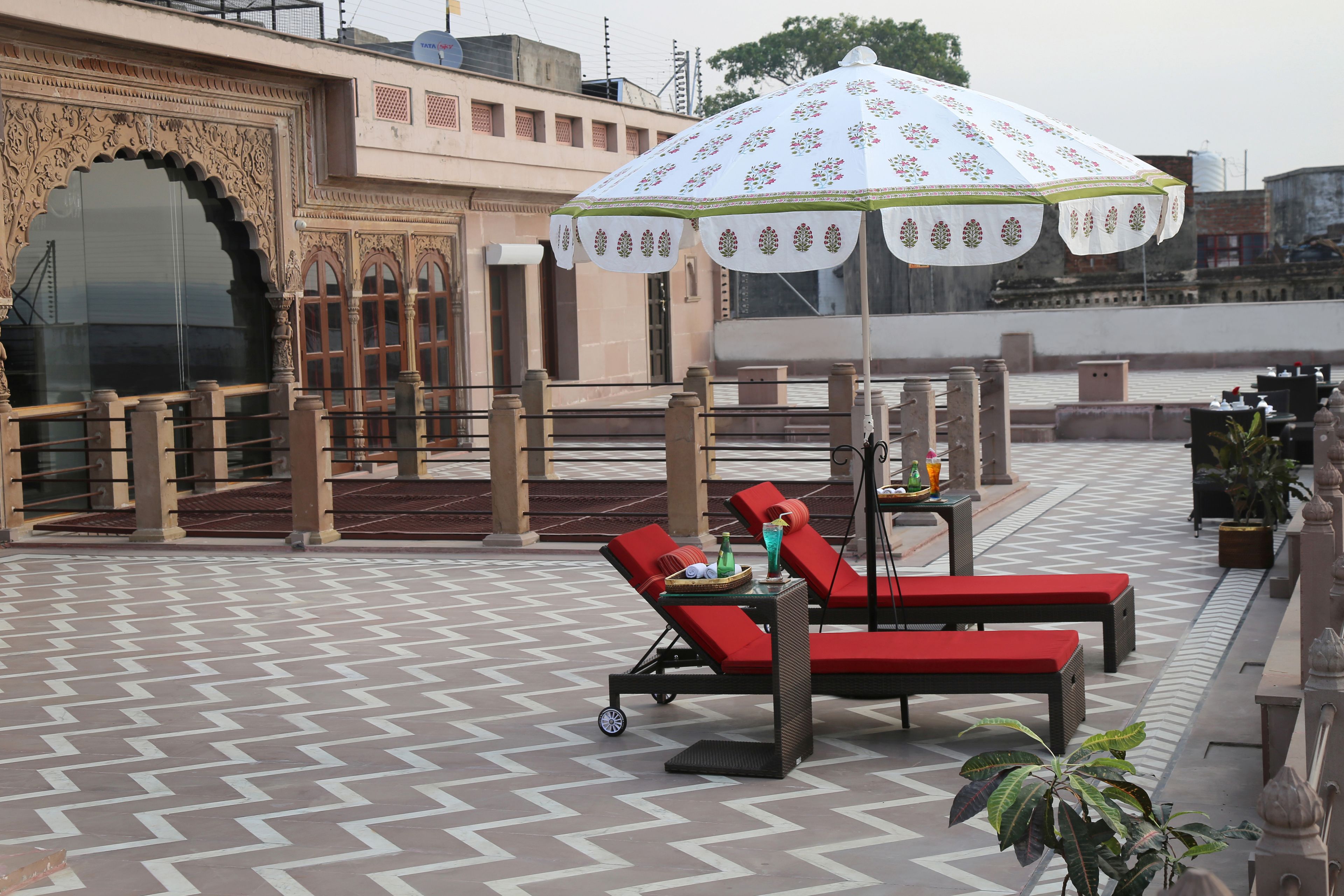 A rooftop lounge area with red lounge chairs, a table with drinks, and a decorative umbrella.