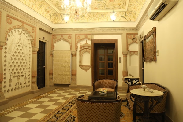 A room with a checkered floor, a patterned sofa, a round table, and a decorative wall with a chandelier.
